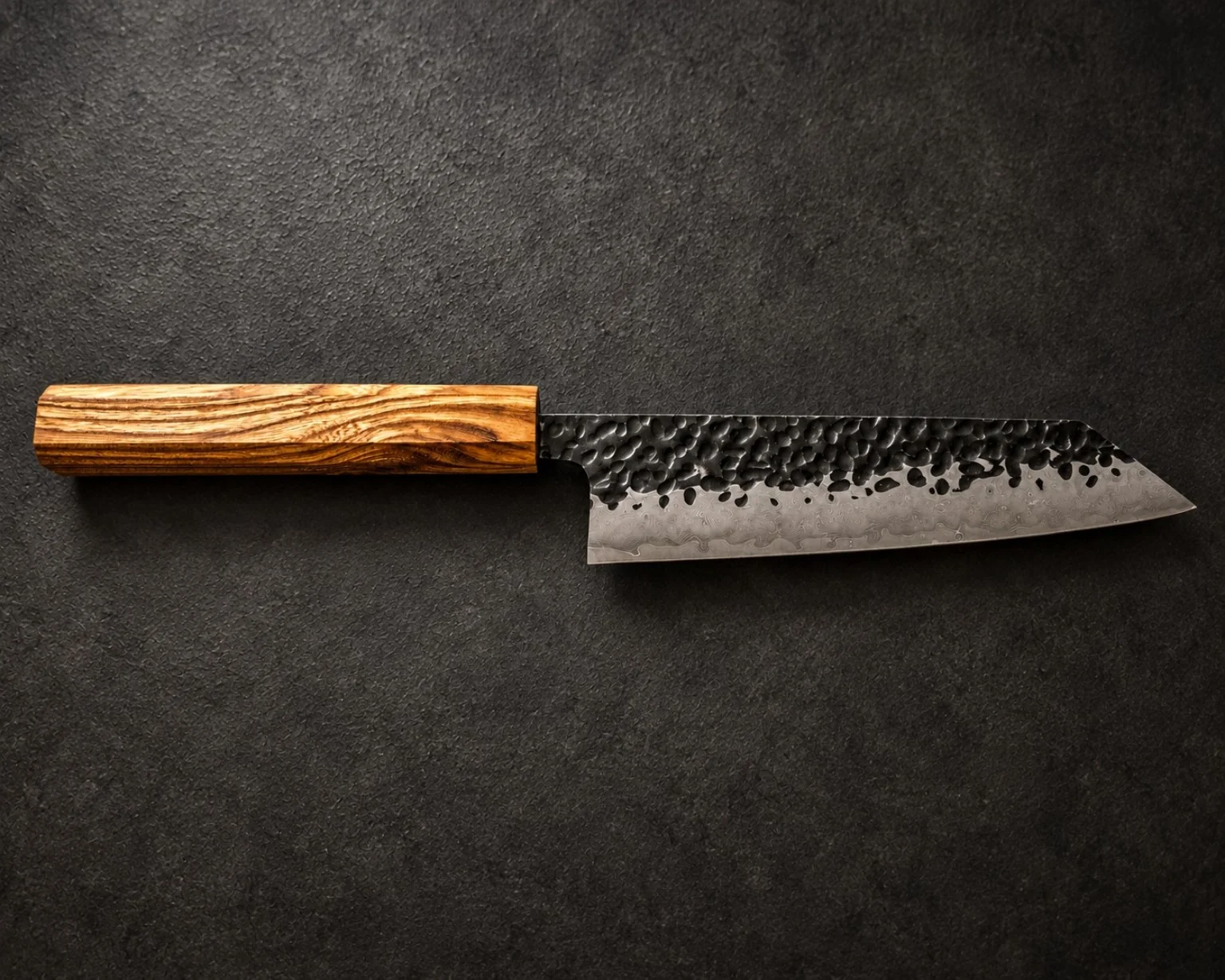 Full-length Japanese-profile knife with a warm striped timber handle on dark textured backdrop